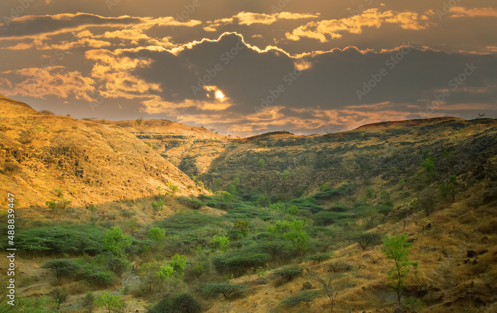 Sunset sky, sunlit clouds, old crumbling mountains and a dry river bed