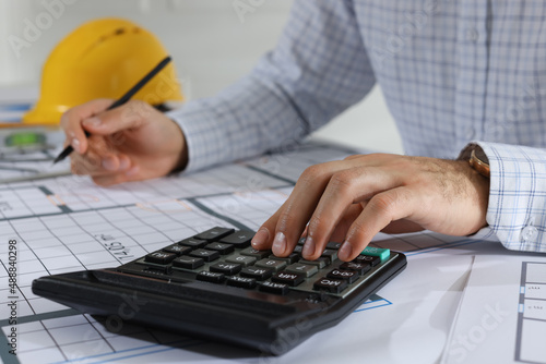 Architect working with construction drawings and calculator indoors, closeup