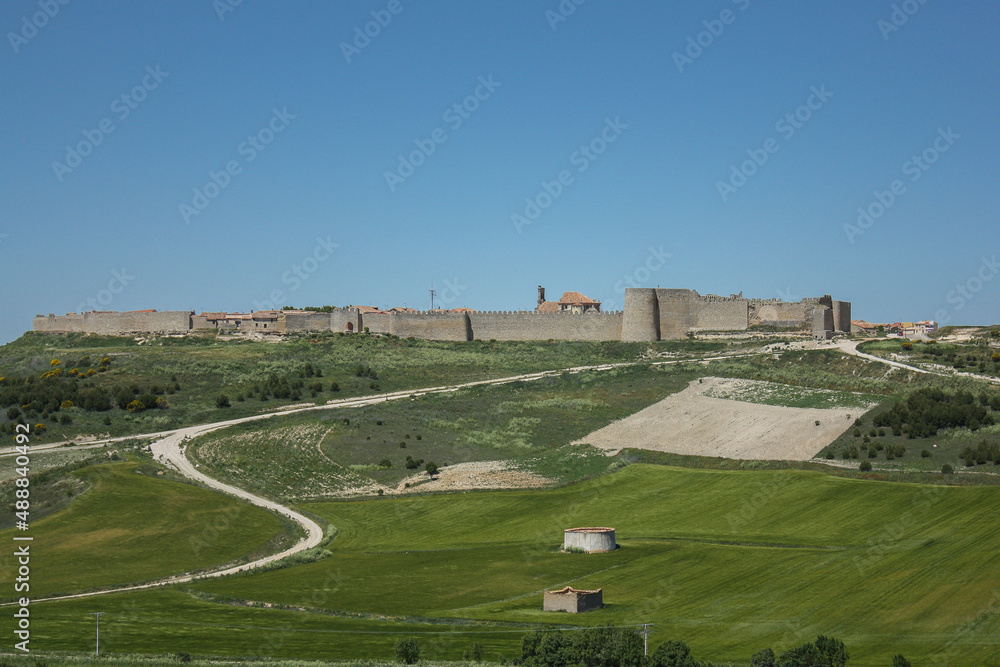 Sinuous road heading to the green hill with the walled city of Urueña in the background on a sunny spring day
