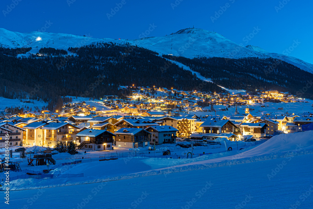 View of Italian village Livigno during twilight. Ski resort in winter time with snowcapped mountains and ski slopes in background