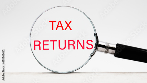 tax returns text through a magnifying glass on a light background © Ihar