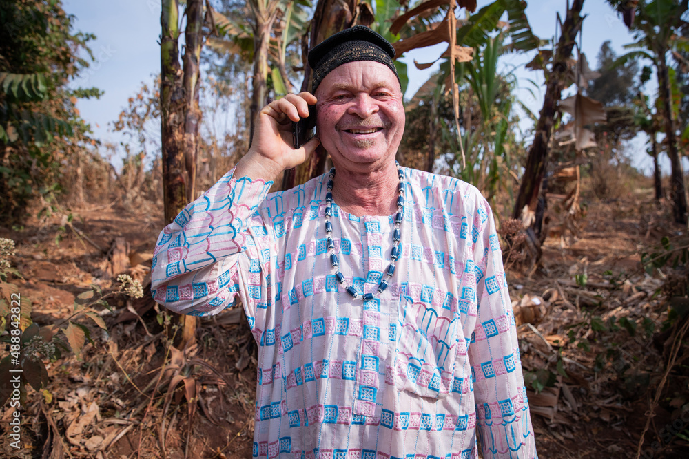 Obraz premium African albino senior makes a phone call and is happy. Man with albinism syndrome dressed in traditional African clothes.