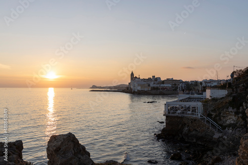 Sitges, Barcelona, Spain - December 20, 2021. People sit at tables in cafes and admire the sunset. Sunset over the Mediterranean. Evening city, sea and sunset.