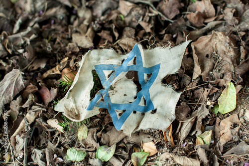 Torn fragment of the blue Star of David from the flag of the State of Israel lies on the ground on a bed of dried leaves. photo