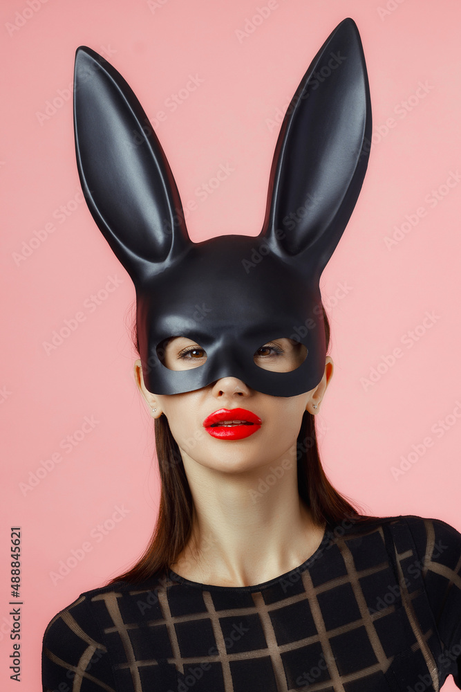 Sexy woman wearing a black mask Easter bunny standing on a pink background and looks very sensually Sexy woman wearing a black mask Easter bunny standing on a pink background and looks very sensually