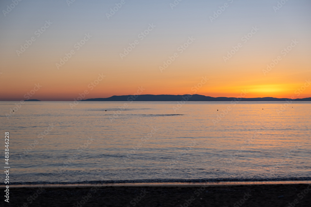 Sandy beach at sunset. Greece. Calm sea water, small ripple, orange color sky.