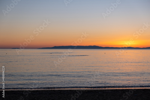 Sandy beach at sunset. Greece. Calm sea water  small ripple  orange color sky.