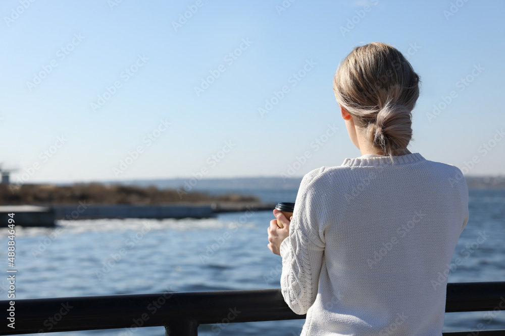Lonely woman with cup of drink near river on sunny day, back view