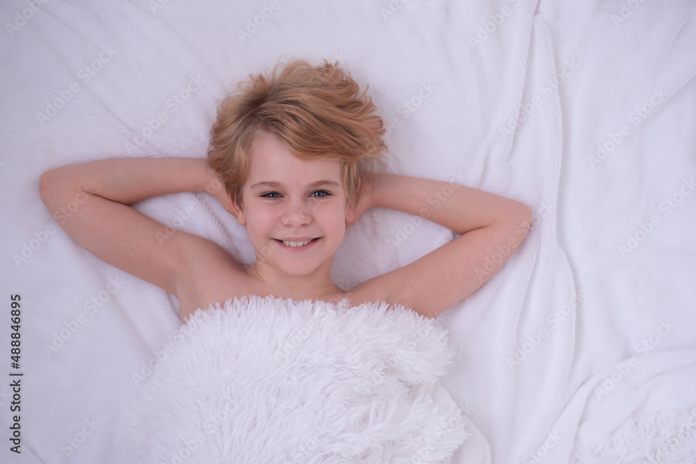 A beautiful teenage girl is lying in bed. Happy child smiles. The concept of good sleep and pleasant awakening. White fluffy blanket. There is space for text. Sincere emotions A beautiful teenage girl is lying in bed. Happy child smiles. The concept of good sleep and pleasant awakening. White fluffy blanket. There is space for text. Sincere emotions