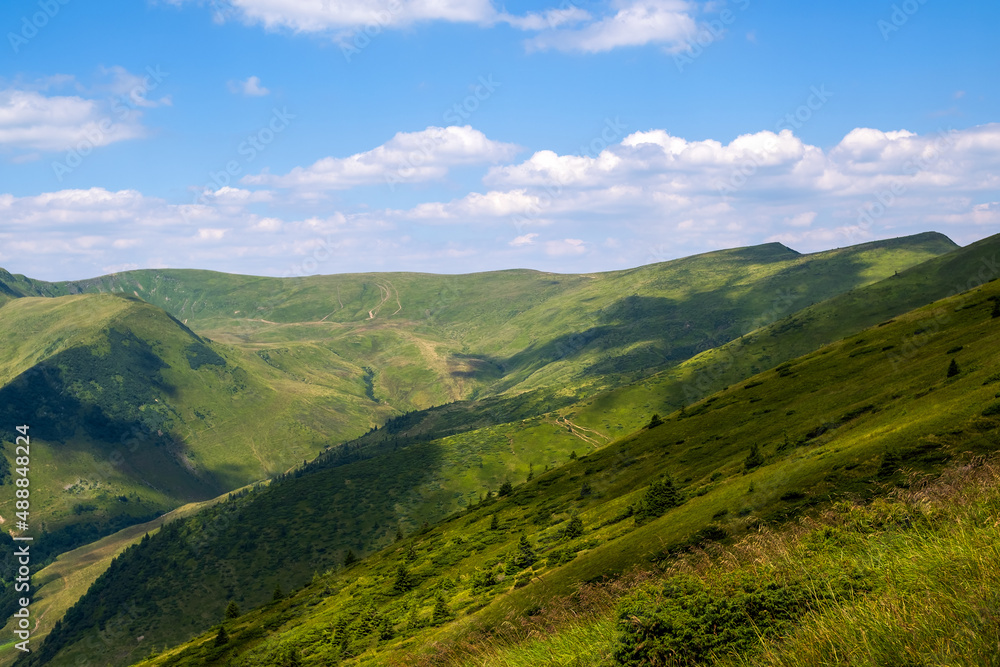 Fototapeta premium Bright landscape with grassy green meadow and distant mountain hills in summer