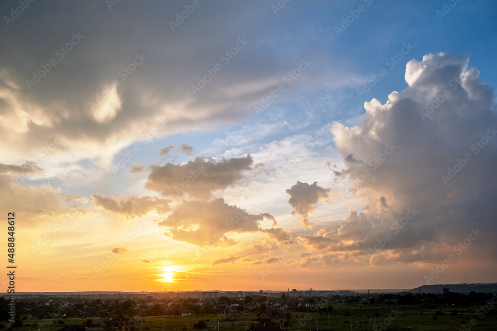 Dramatic sunset landscape with puffy clouds lit by orange setting sun and blue sky
