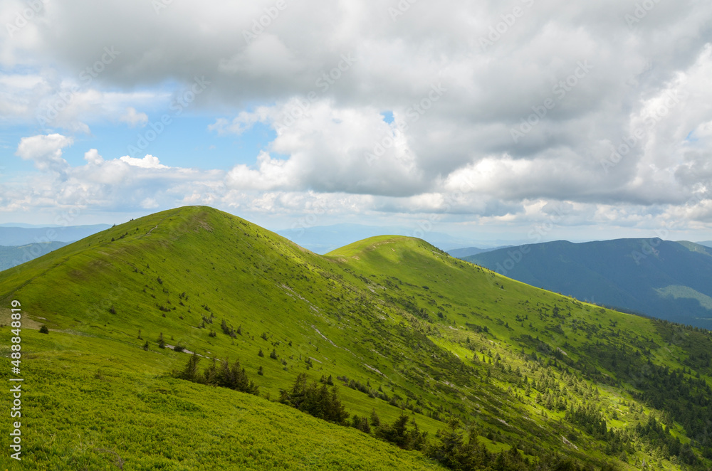 Hiking trail through mountain ridge with high peaks covered green grass under cloudy sky. Carpathian Mountains, Ukraine Hiking trail through mountain ridge with high peaks covered green grass under cloudy sky. Carpathian Mountains, Ukraine