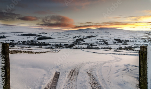 A track leading into a snowy field, against a golden, early evening sky in the North Pennines, Weardale, County Durham