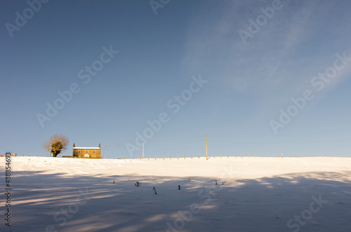 A lone house stands at the top of a snow covered, sunny hill in the North Pennines, Weardale, County Durham photo