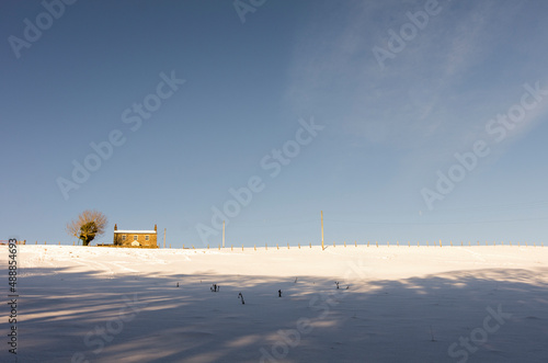 A lone house stands at the top of a snow covered, sunny hill in the North Pennines, Weardale, County Durham
