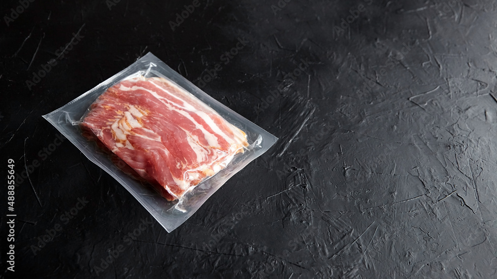 Bacon strips, raw smoked pork meat slices in vacuum package on black table
