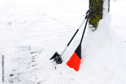 snowy field, black snow shovel and plastic broom supported against a tree trunk