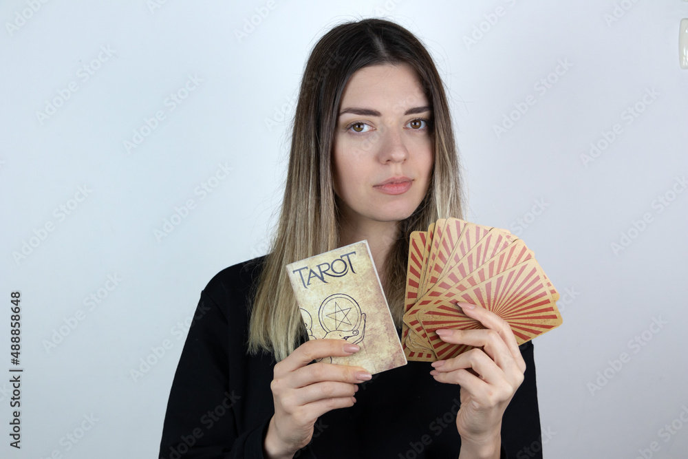 Young woman with casual clothes holding tarot book and tarot cards. White isolated background. Young woman with casual clothes holding tarot book and tarot cards. White isolated background.