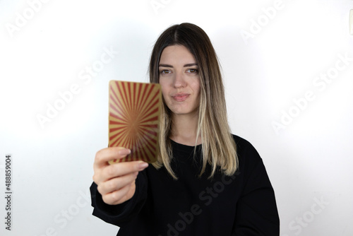 Young woman with casual clothes holding magical card and showing it to the camera. She is so happy and smiling. Tarot card. Photo taken is white isolated background.