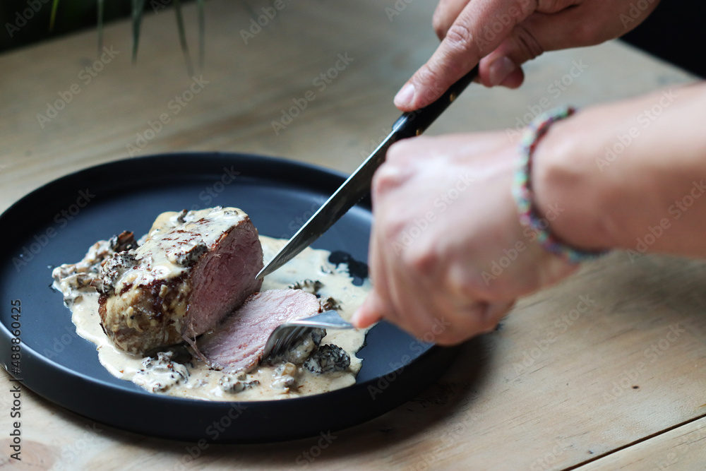 Hands cutting steak on black plate and wood table Hands cutting steak on black plate and wood table