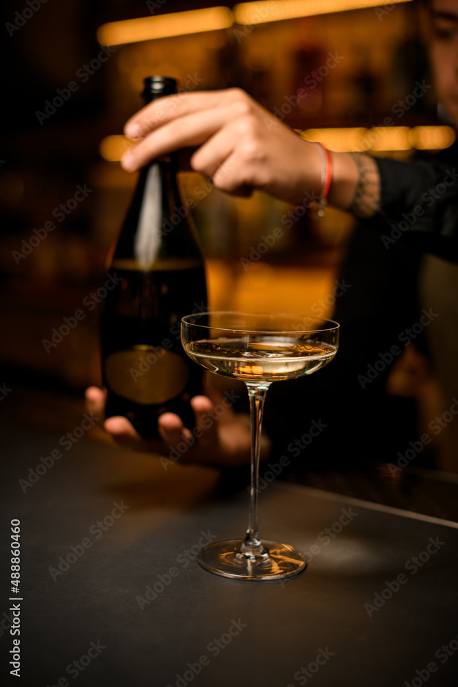 beautiful wine glass with drink on bar. Hand of a man bartender with a bottle in the background