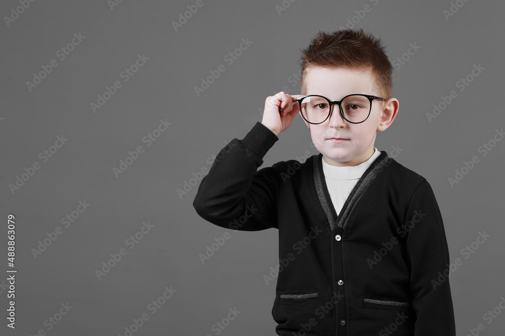 Smart child boy adjusts his glasses with finger on the grey background, close-up. Studio juvenile portrait in casual clothes. copy space