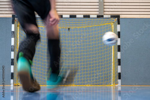 Junge schießt in einer Sporthalle mit seinem Fußball ein Tor photo