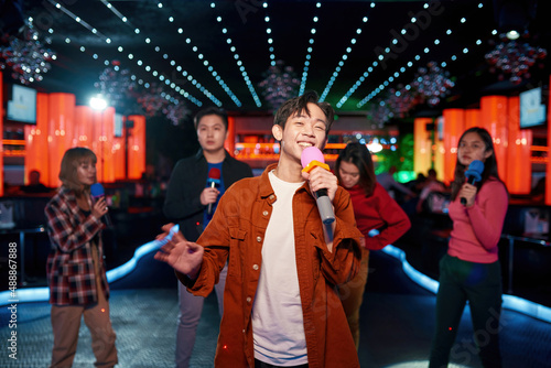 Asian young guy with friends dancing and singing at karaoke bar