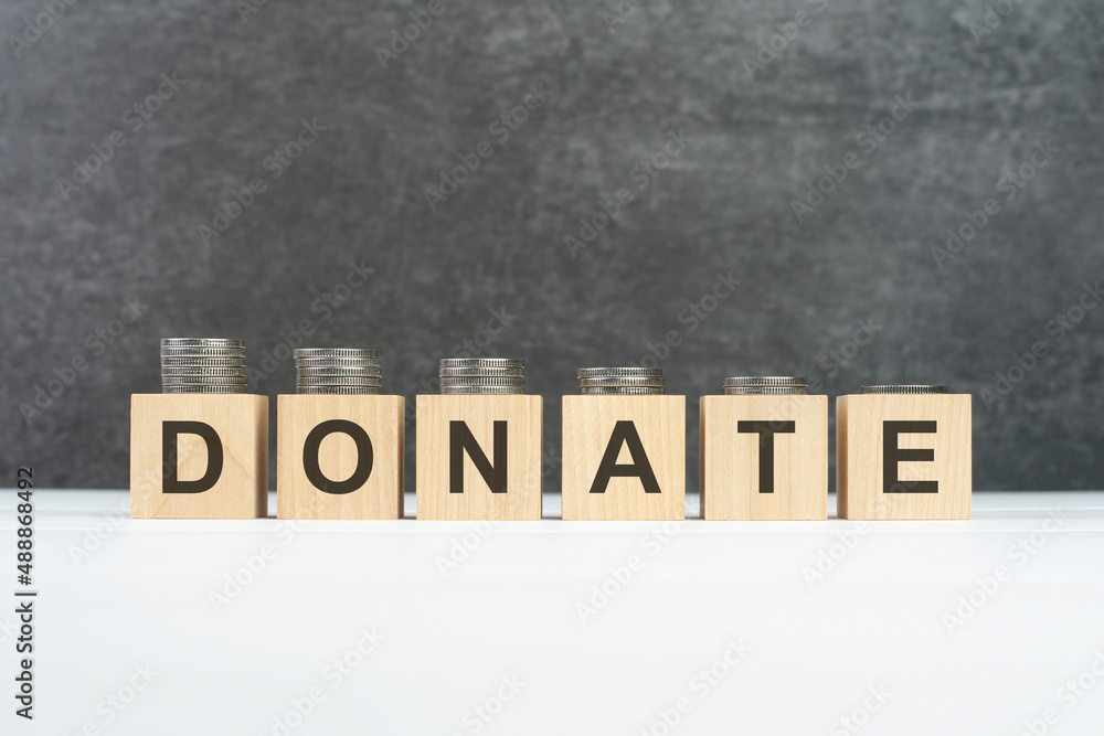 DONATE word, text written on wooden cubes on a black background with coins on cubes DONATE word, text written on wooden cubes on a black background with coins on cubes