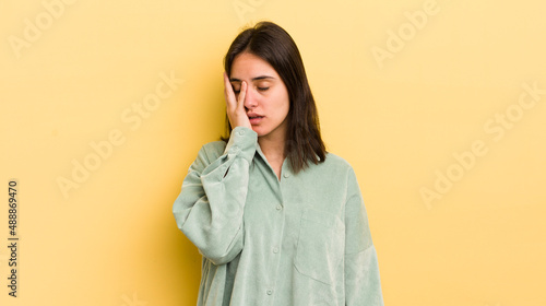young hispanic woman feeling bored, frustrated and sleepy after a tiresome, dull and tedious task, holding face with hand