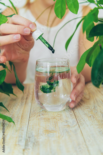 Woman dripping chlorophyll supplement into a glass of water. Selective focus. photo