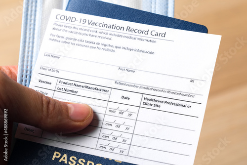Passport with COVID-19 Vaccination record card and medical mask in hand. Close up view. - Image