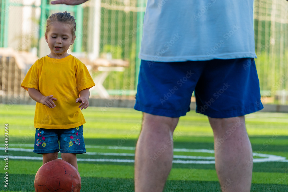 Cute little girl in yellow t-shirt going to kick the ball to father. Cute little girl in yellow t-shirt going to kick the ball to father.