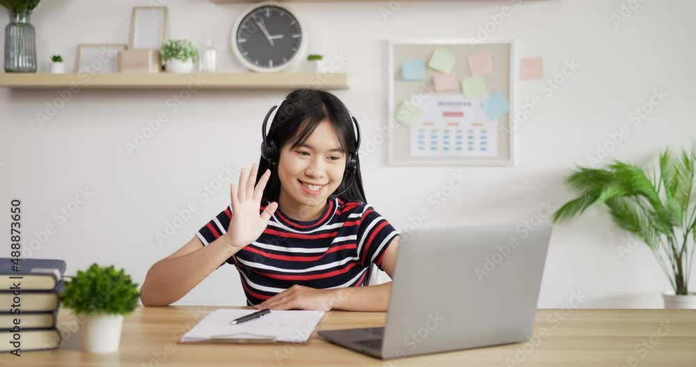 Portrait of Young Asian customer service support agent telemarketer wearing headset looking at laptop make business conference internet video call. Woman waving hand and making note. Portrait of Young Asian customer service support agent telemarketer wearing headset looking at laptop make business conference internet video call. Woman waving hand and making note.
