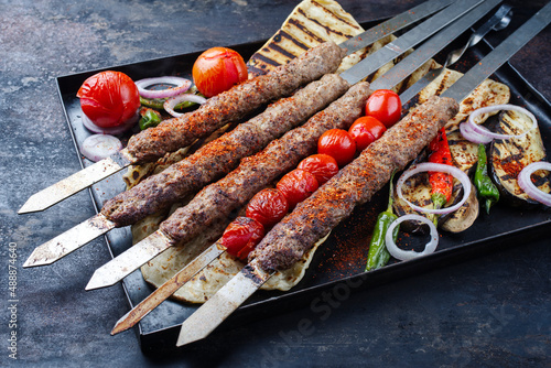 Traditioneller türkischer Adana Kebap am Schaschlik Spieß mit Grillgemüse und Fladenbrot serviert als close-up auf einem rustikalen Metall Tablett photo