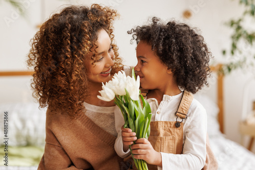 Grateful ethnic mother with bouquet hugging son