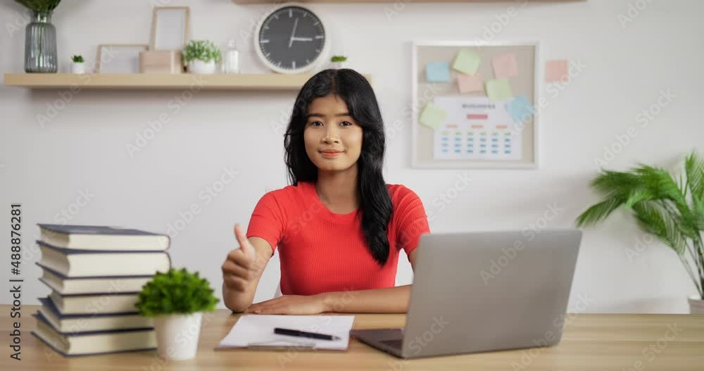 Portrait of Asian schoolgirl studying online via laptop showing thumb up at home. Distance learning and education concept. Portrait of Asian schoolgirl studying online via laptop showing thumb up at home. Distance learning and education concept.