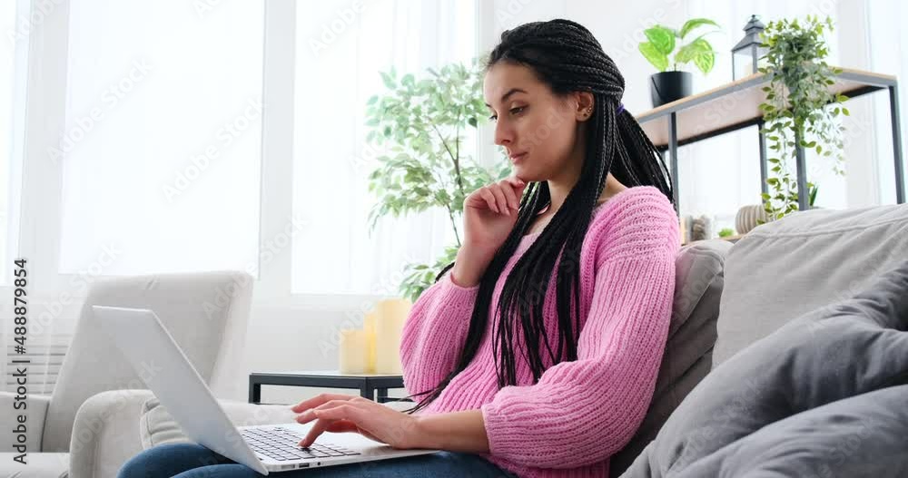 Young woman typing laptop sitting on sofa at home Young woman typing laptop sitting on sofa at home