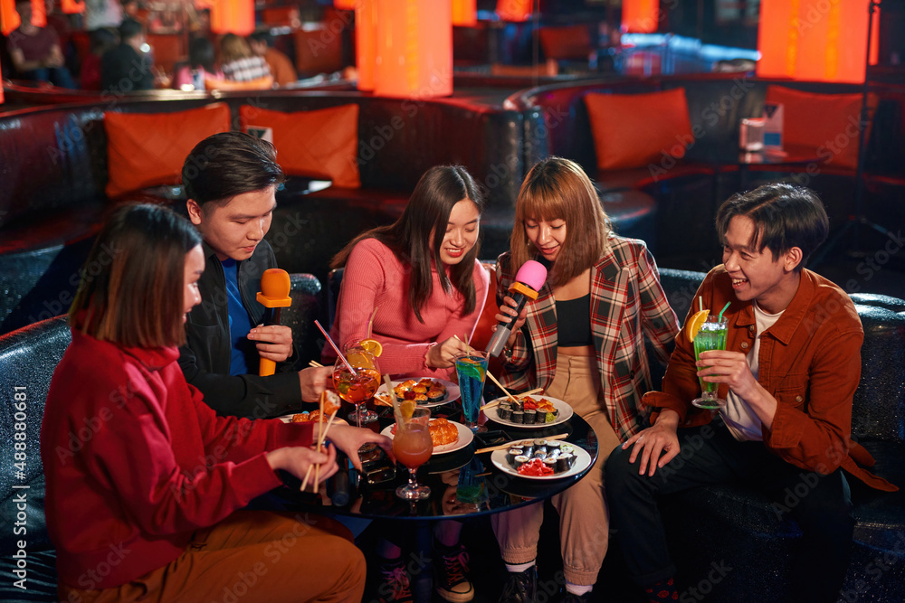 Group of asian guys and girls singing songs and eating sushi at karaoke club Group of asian guys and girls singing songs and eating sushi at karaoke club