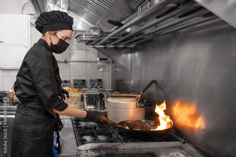 Woman Chef in protective face mask prepare food in the kitchen of a restaurant or hotel during new normal. Coronavirus prevention concept. High quality photo Woman Chef in protective face mask prepare food in the kitchen of a restaurant or hotel during new normal. Coronavirus prevention concept. High quality photo
