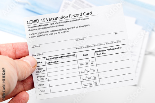 Womans hand holds coronavirus vaccination record card on background blue medical mask. Concept of defeating Covid-19 - Image