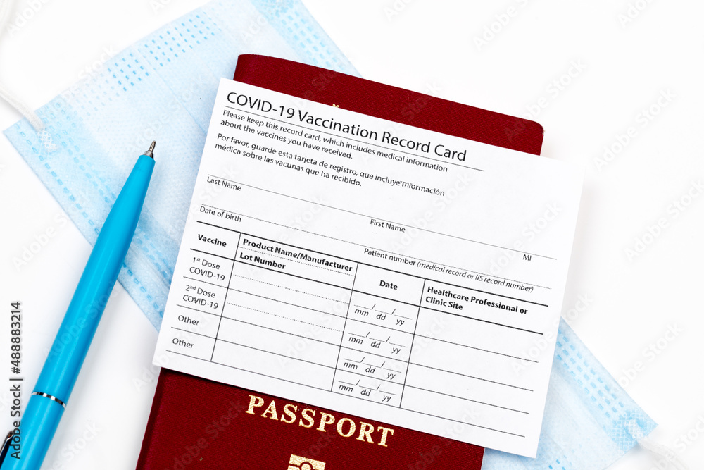 Coronavirus vaccination record card, biometric passport and blue medical mask on light gray desk. Concept of defeating Covid-19. Vaccination as prerequisite for travel - Image Coronavirus vaccination record card, biometric passport and blue medical mask on light gray desk. Concept of defeating Covid-19. Vaccination as prerequisite for travel - Image