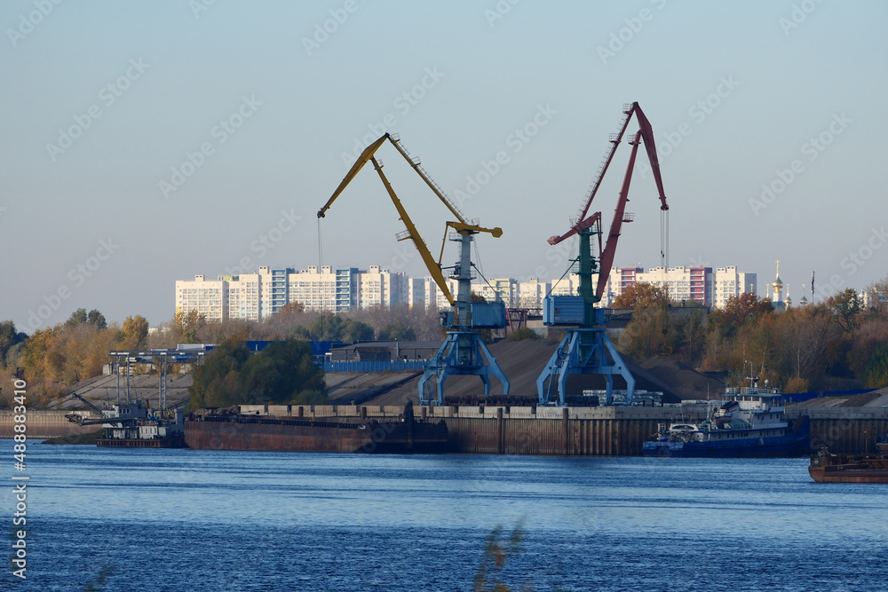 River port. Construction site on the river bank. A harbor crane loads sand onto a barge.