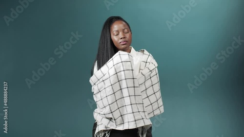 An illness african woman in a white scarf stands crossing her arms and sneezes