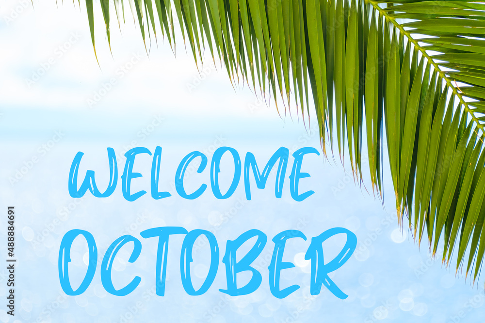 Welcome October text on the background with palm leaf and blue sea. Template of a greeting card, postcard or advertisement of a tour agency. 