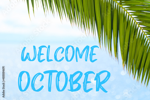 Welcome October text on the background with palm leaf and blue sea. Template of a greeting card, postcard or advertisement of a tour agency. 