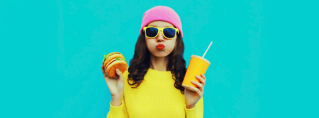Portrait of stylish young woman with burger and cup of juice fast food on blue colorful background
