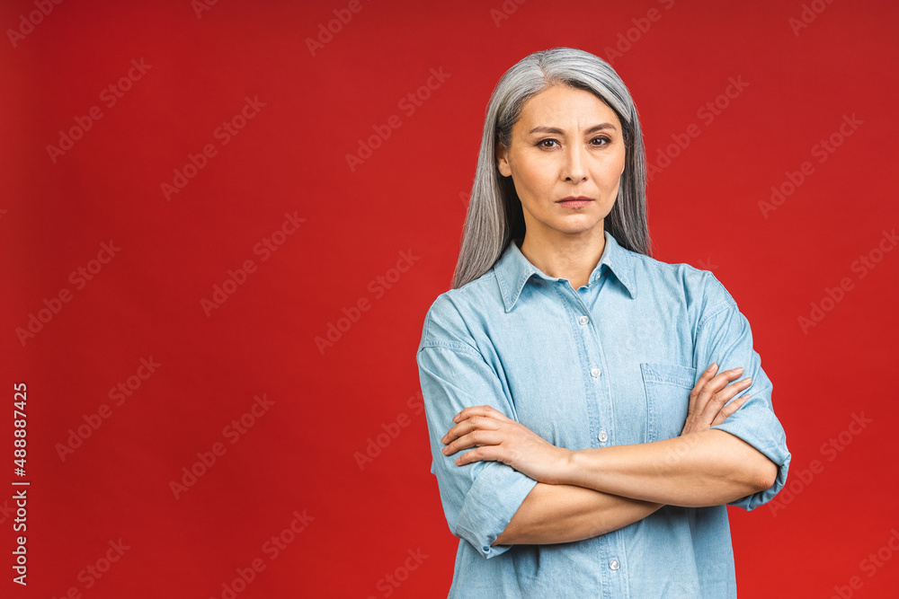 Serious angry elegant mature senior aged asian business woman smiling standing isolated over red background. Smiling confident cheerful middle aged lady, copy space.