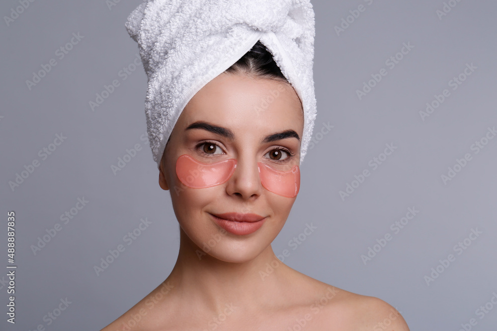 Beautiful young woman with under eye patches and hair wrapped in towel on grey background Beautiful young woman with under eye patches and hair wrapped in towel on grey background