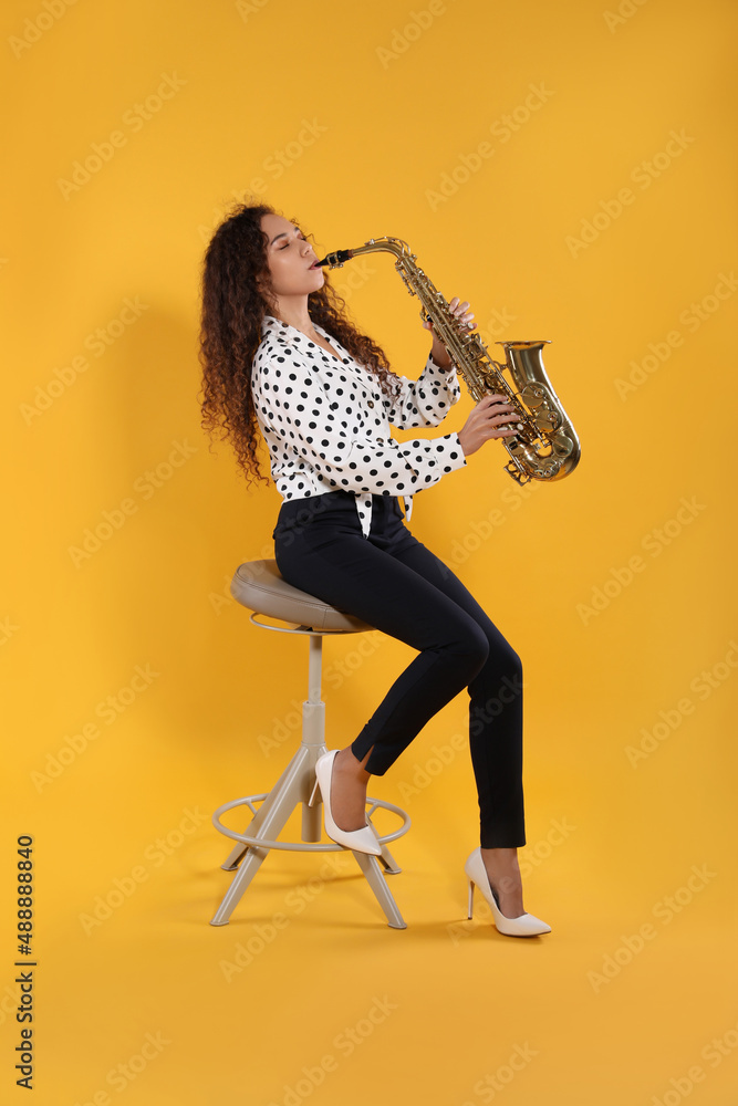 Fototapeta premium Beautiful African American woman playing saxophone on yellow background